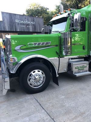 Green semi-truck parked in front of a building with chrome accents. 
