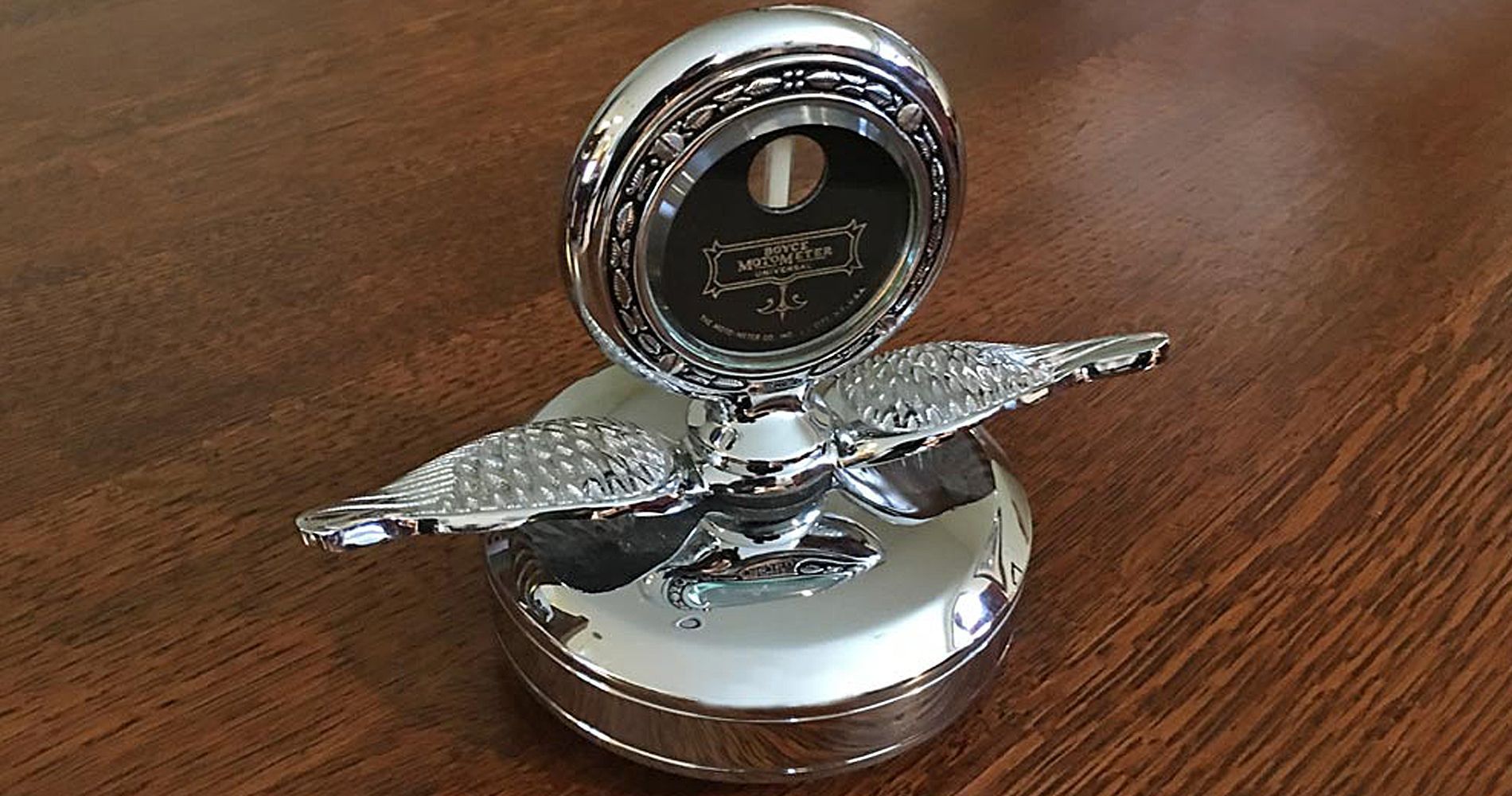 Chrome car hood ornament with winged emblem, atop a wooden table.