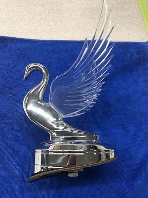 Chrome swan car hood ornament with clear plastic wing, set on a dark blue cloth.