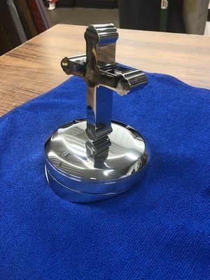 Shiny chrome cross on a circular base, sitting on a blue cloth.