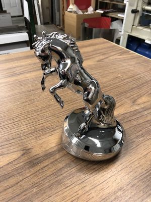 Shiny chrome horse statue rearing up on a circular base, on a wooden surface.