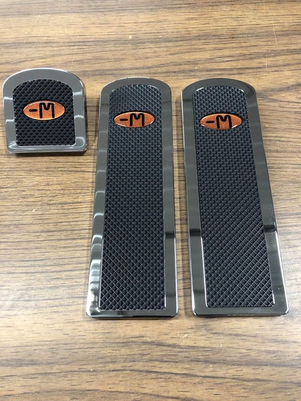 Three black metal car pedal covers, with an orange 