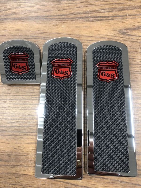 Chrome G&S logo foot pedals on a wood surface.  Black textured centers, red logos.