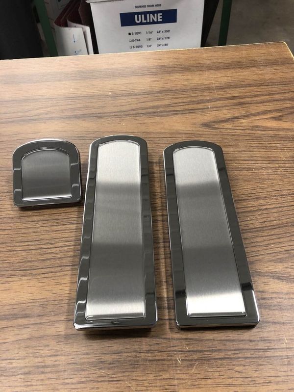 Three polished metal plates on a wooden surface; one small and two long rectangular with rounded tops.