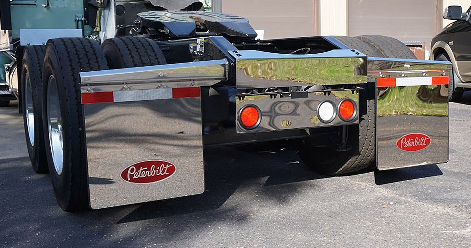 Rear view of a semi-truck with polished chrome fenders, tires, and lights, on a paved surface.
