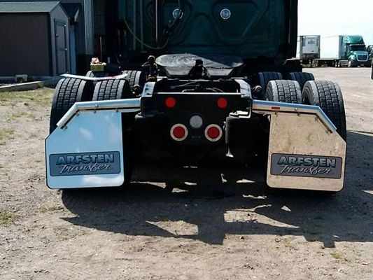 Rear view of a semi-truck with chrome fenders, mud flaps, and taillights, parked on gravel.