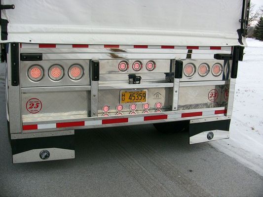 Rear view of a semi-trailer with red and white reflective tape, multiple lights, and a license plate.