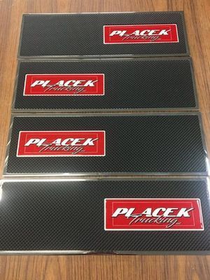 Four Placek Racing carbon fiber-style license plates with red and white logos on a wooden surface.