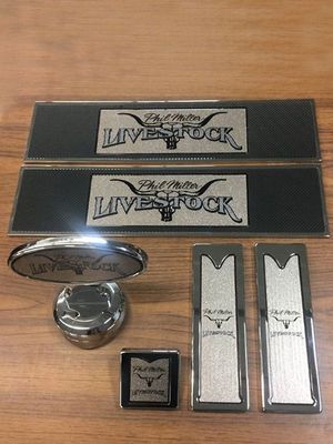 Silver and black branded automotive accessories, including license plates and trim pieces, on a wooden surface.