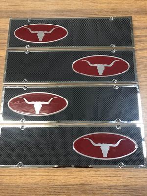 Four rectangular license plate frames with red oval logos featuring a longhorn steer head on a black, carbon-fiber pattern.