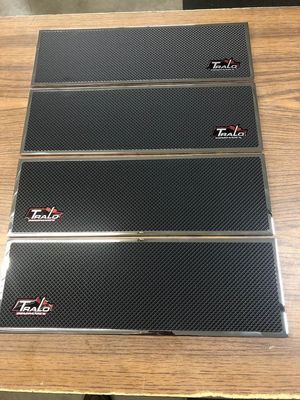 Four rectangular black carbon fiber-like mats with a metallic border and logo on each.