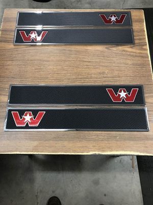 Four Western Star truck step plates with red and white logos on a wooden surface.