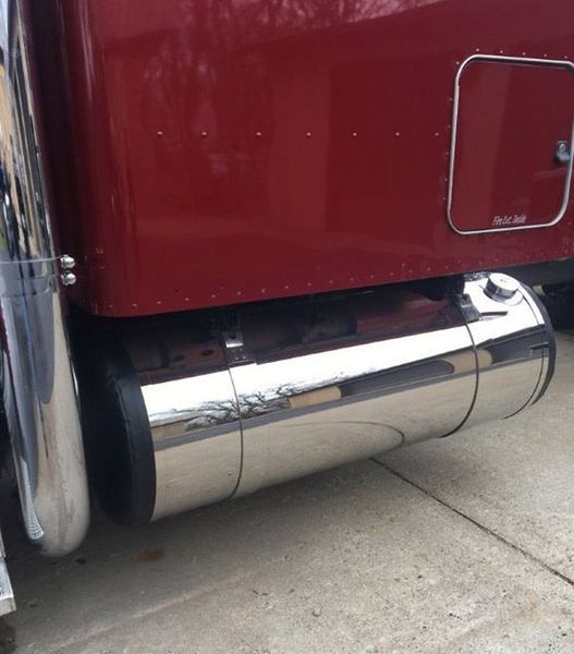 Shiny chrome fuel tank on a maroon semi-truck, parked on a concrete surface.