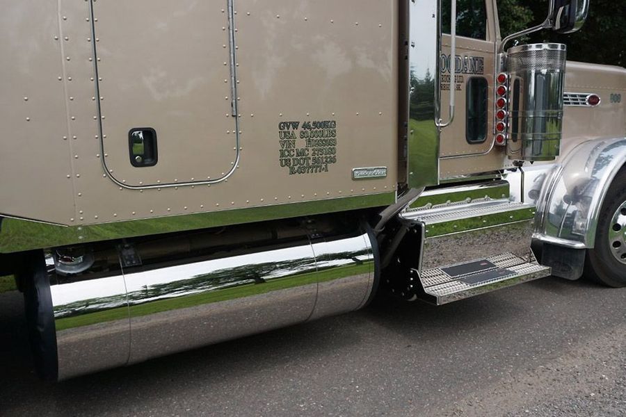 Side view of a beige semi-truck with chrome accents and steps outdoors.