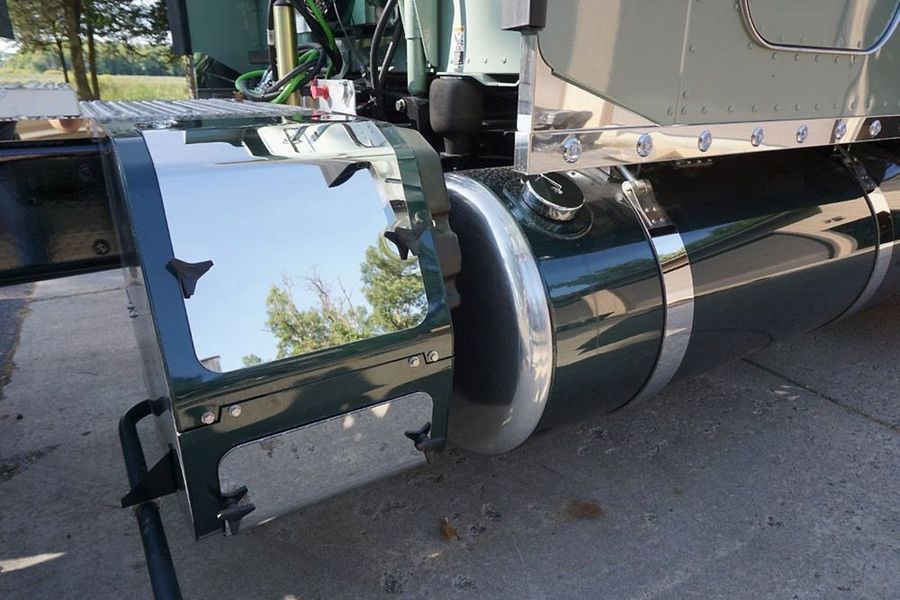 Shiny chrome mud flap and fuel tank on a green semi-truck, reflecting the surroundings.
