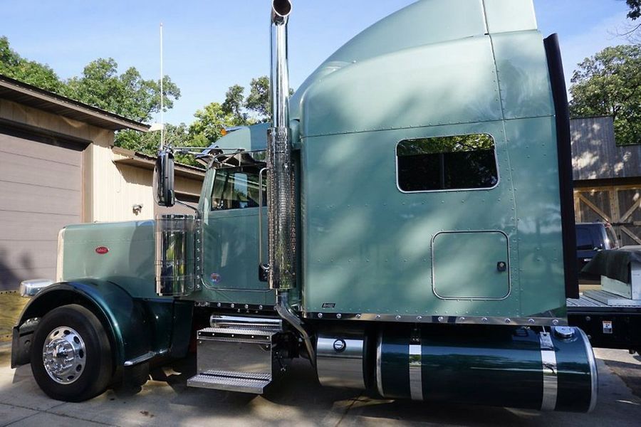 Green semi-truck parked outdoors, side view. Chrome accents, silver fuel tank, and exhaust pipe.