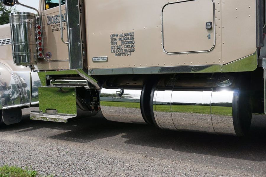 Tan and chrome semi-truck parked on the side of a road, with shiny fuel tank covers.