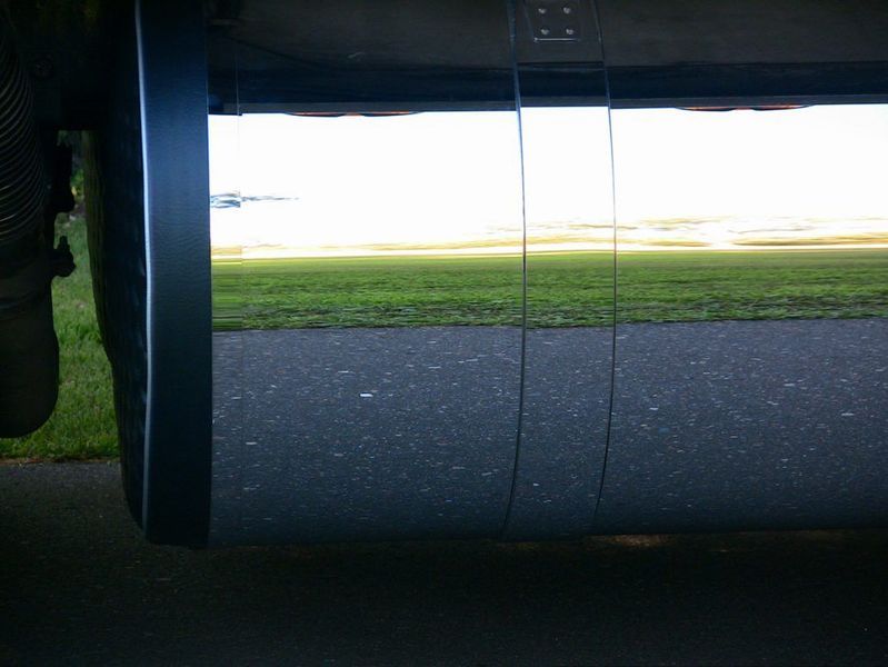 Under view of a large, reflective surface with black asphalt and green grass in the distance.