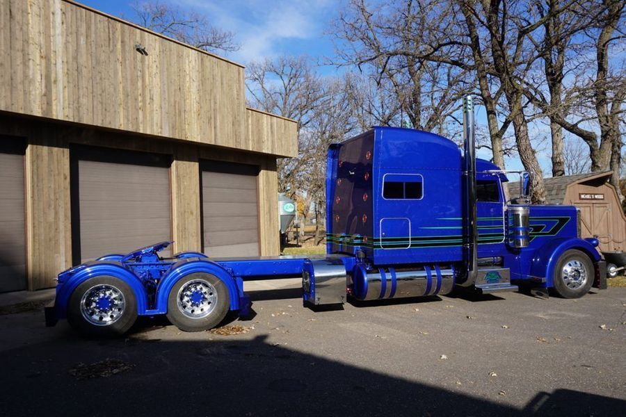 Blue semi-truck with custom fenders parked next to a building.