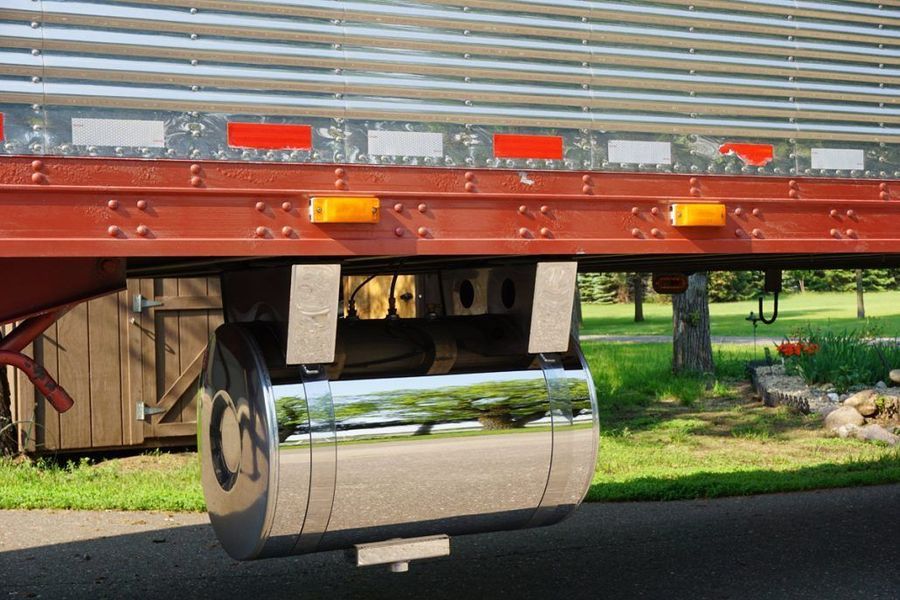 Chrome fuel tank mounted under a red semi-trailer, with reflective markers.