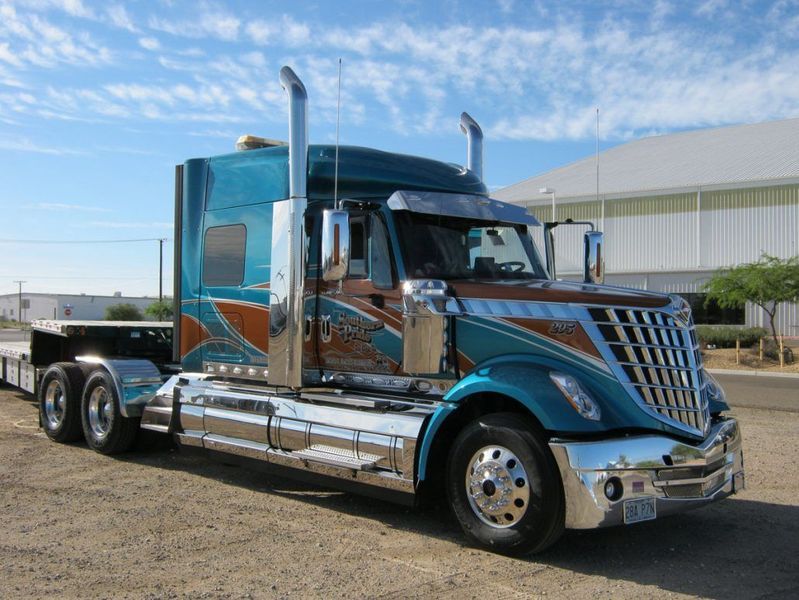 Blue and brown custom semi-truck with chrome accents parked on dirt lot under blue sky.