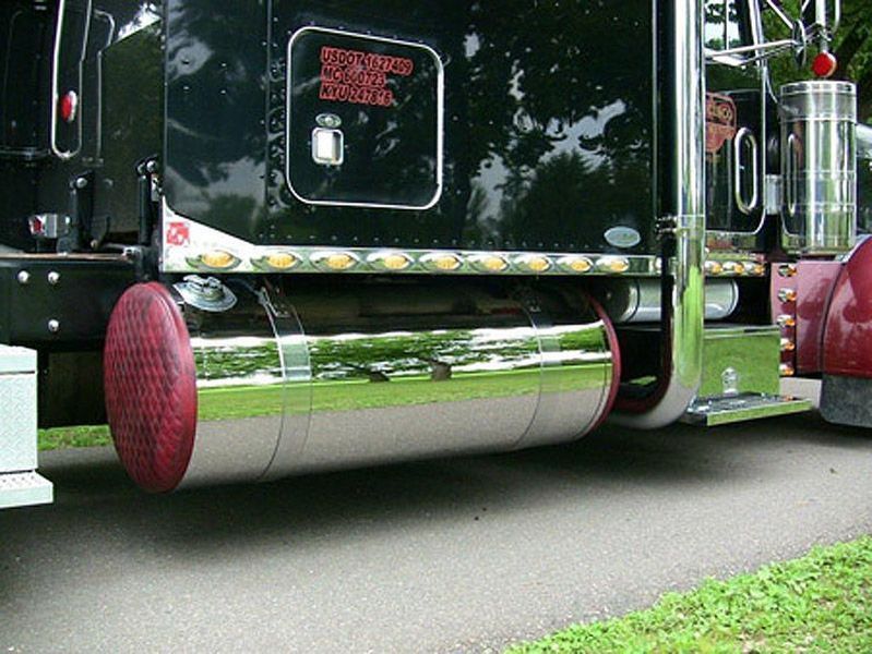 Chrome fuel tank on a black semi-truck, with red ends, parked on pavement.