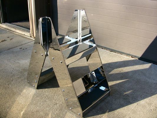 Two reflective, stainless steel A-frame signs outdoors, on concrete, reflecting the surroundings.