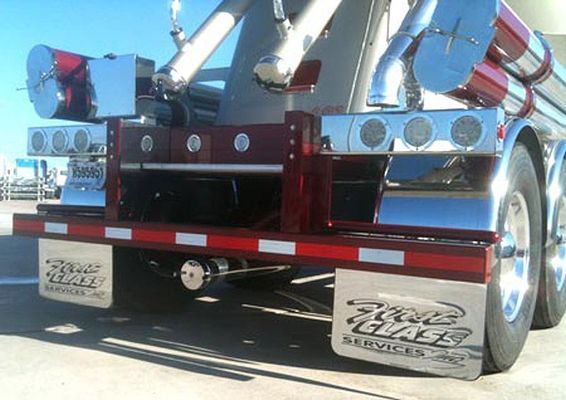 Rear view of a red and chrome tanker truck with white and red reflective tape, and mud flaps with company logo.