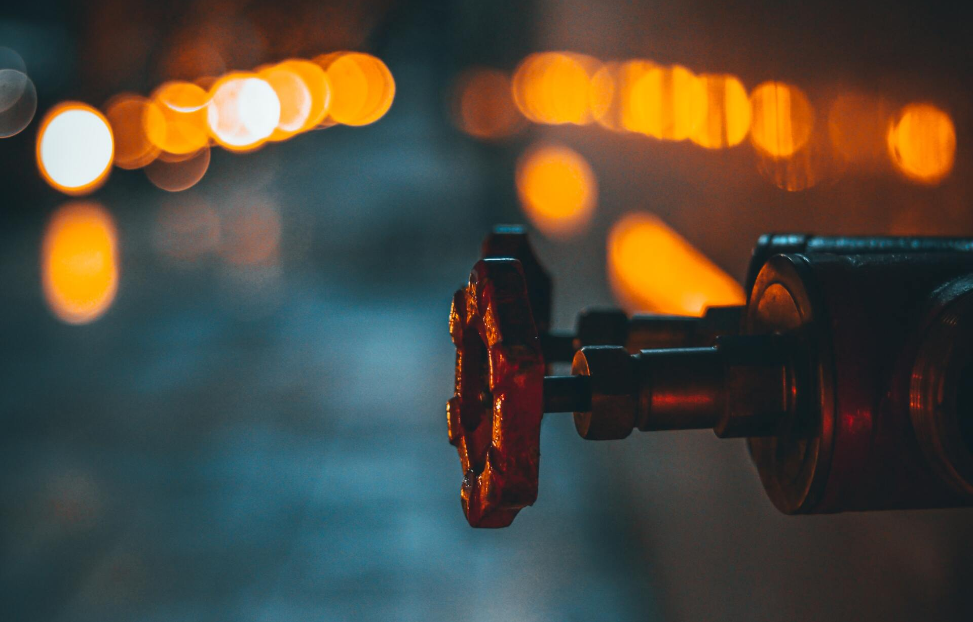 Rusty red valve with orange bokeh lights in background.