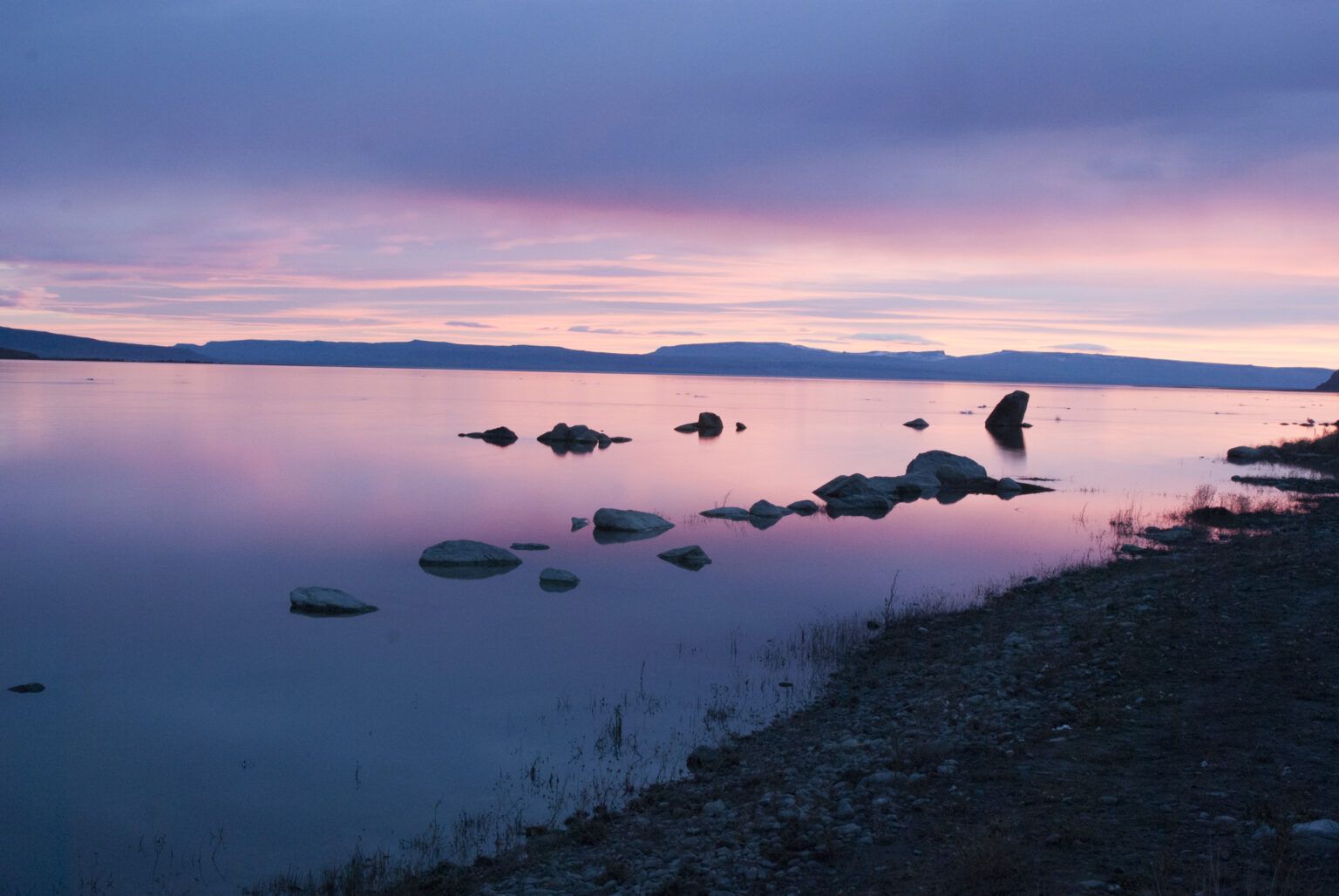 Una puesta de sol sobre un lago con rocas en el agua.