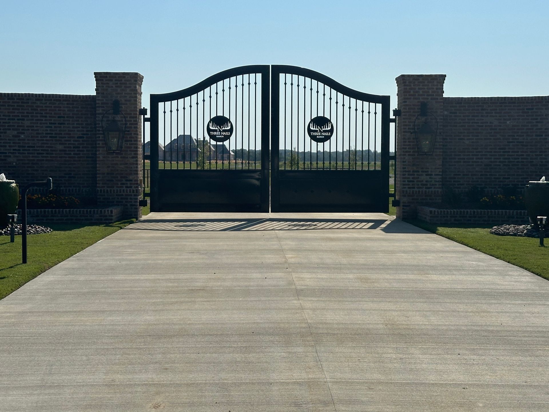 Black wrought-iron gate between brick pillars at the end of a paved driveway