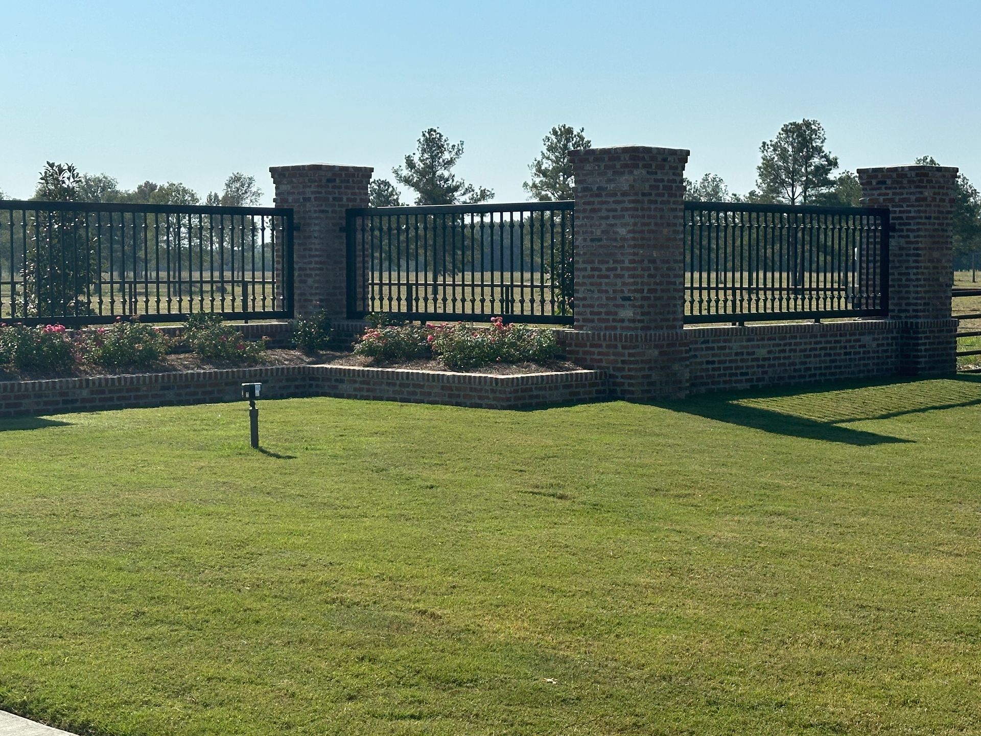 Brick-and-metal fence along a grassy lawn under a clear sky