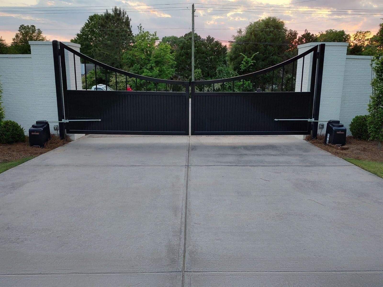 Black driveway gate between white brick pillars at sunset.