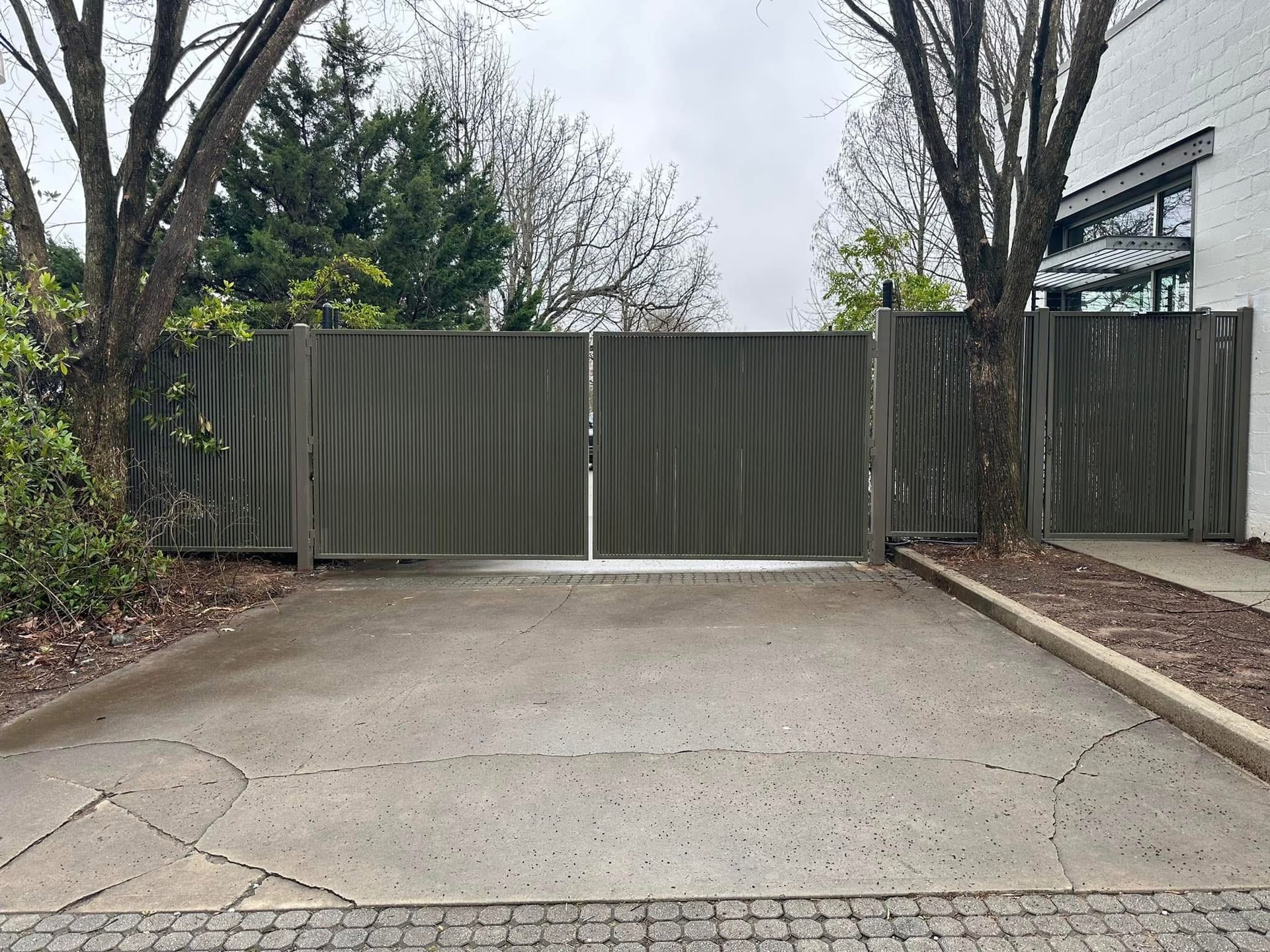 Driveway leading to a closed metal gate between trees and a modern building.