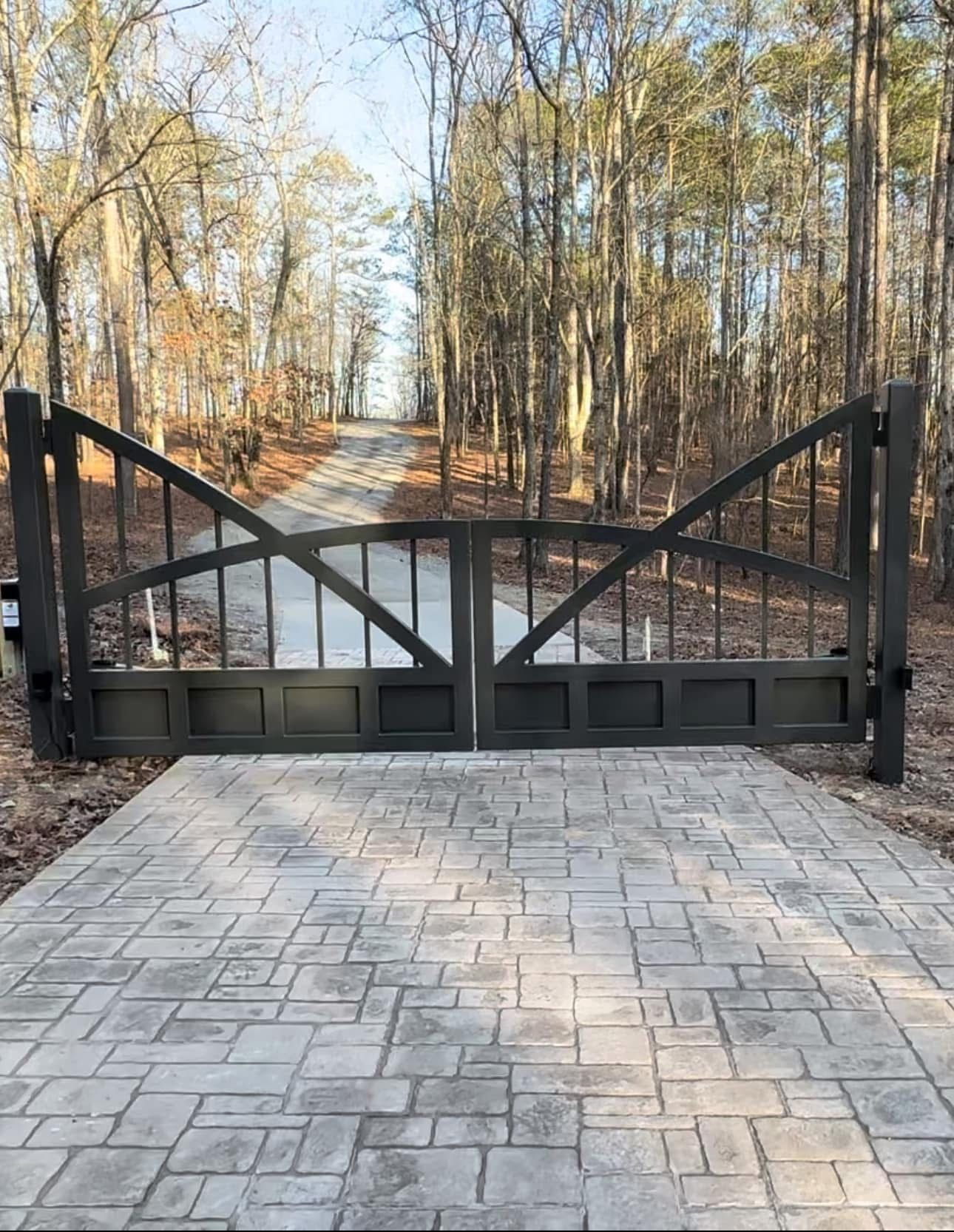 Black metal gate blocking a paved driveway in a wooded area