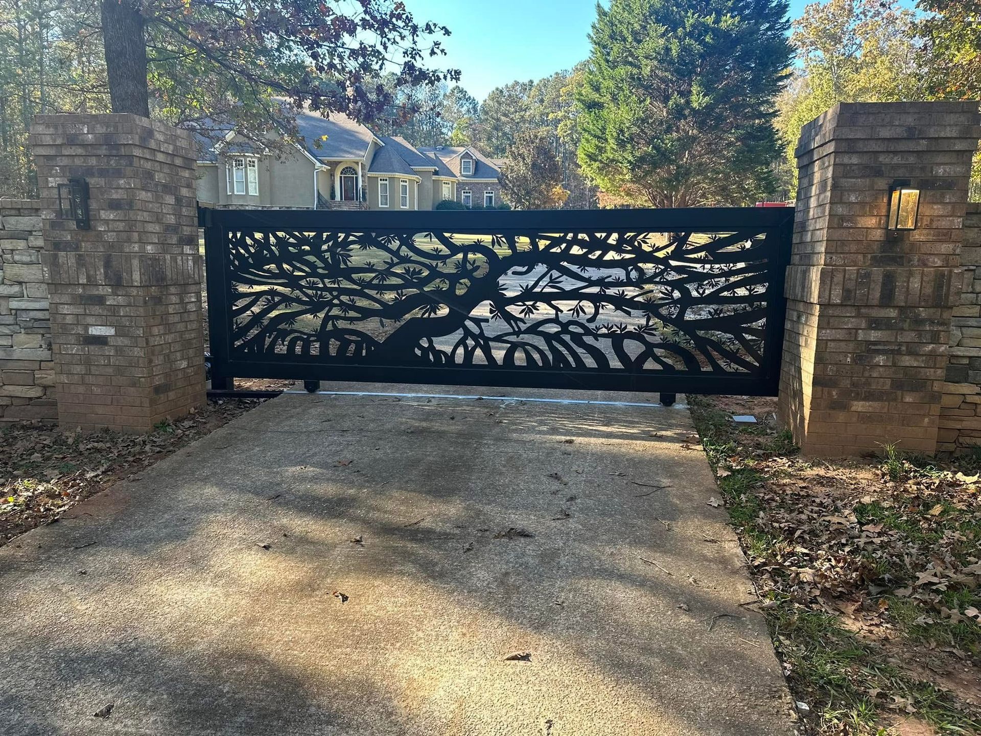 Black metal driveway gate with tree silhouette between stone pillars at a home entrance