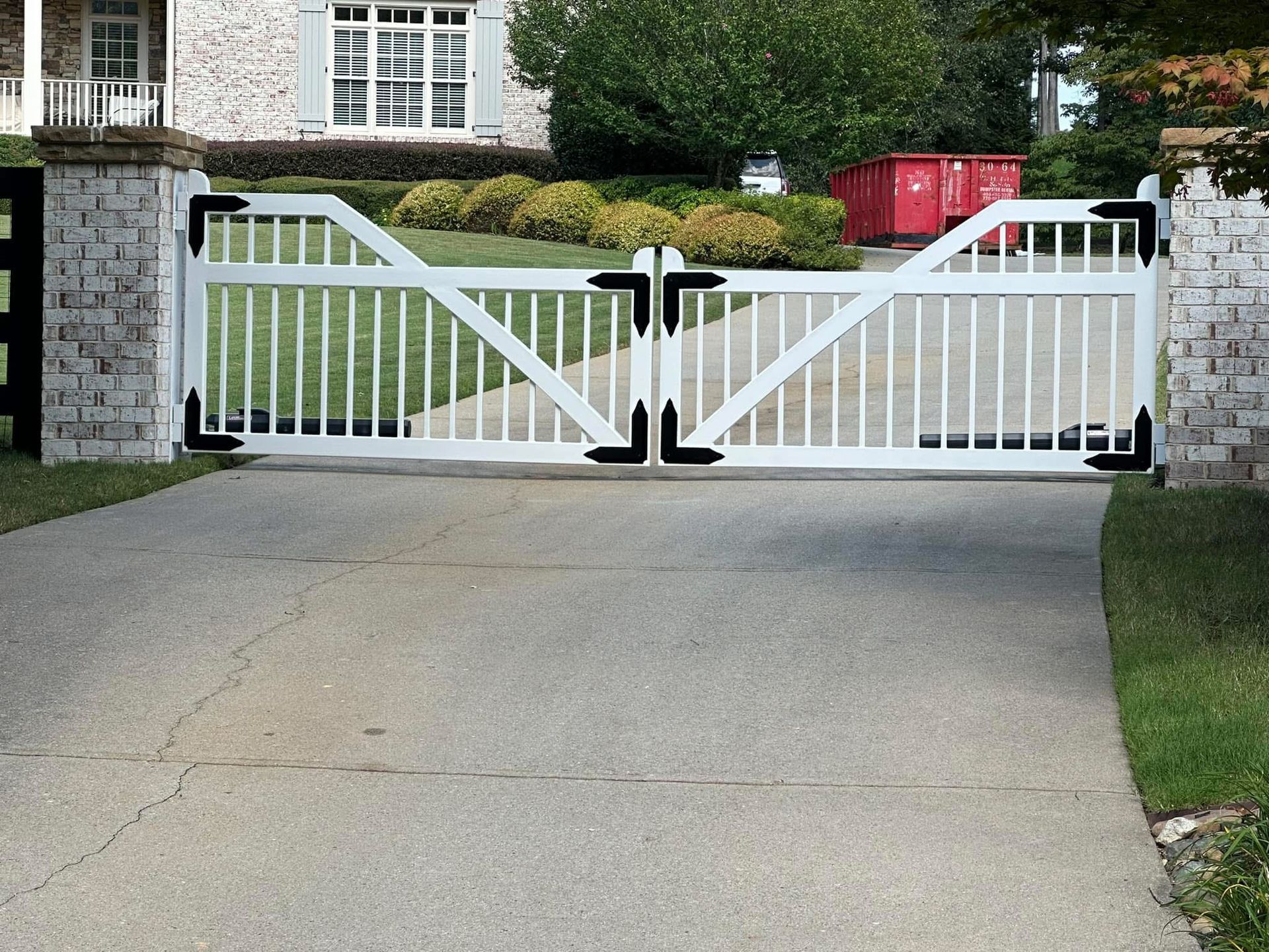 White wooden driveway gate between stone pillars at a suburban home entrance