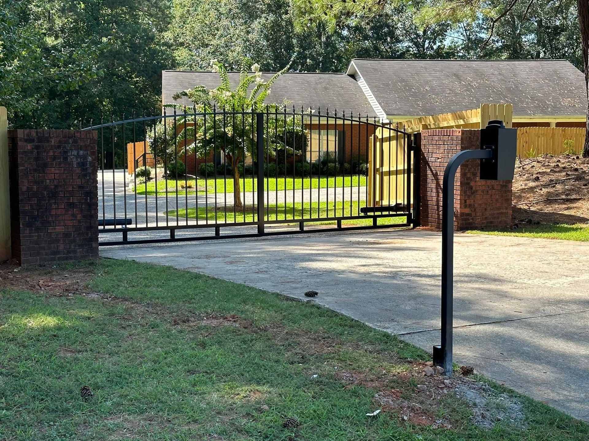 Gated driveway entrance with black metal gate, brick pillars, and mailbox in front of a yellow house