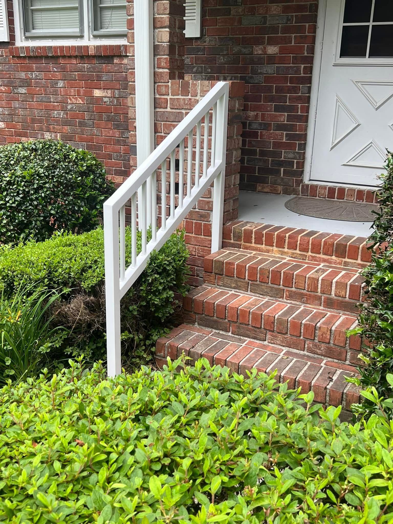 Brick front porch steps with white railing and a screen door, surrounded by green shrubs.
