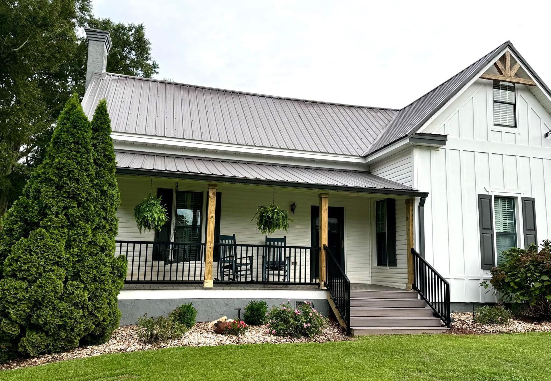 White farmhouse with porch, black railing, and front steps, surrounded by lawn and trees