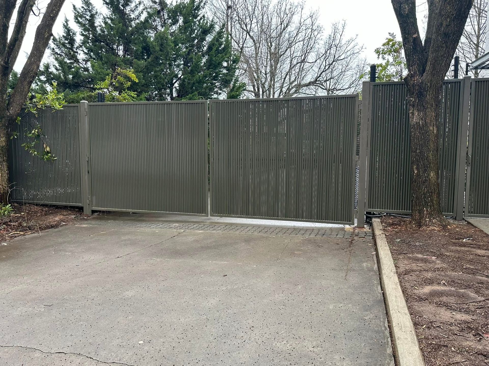Weathered metal gate blocking a driveway, with trees and a concrete curb on either side.
