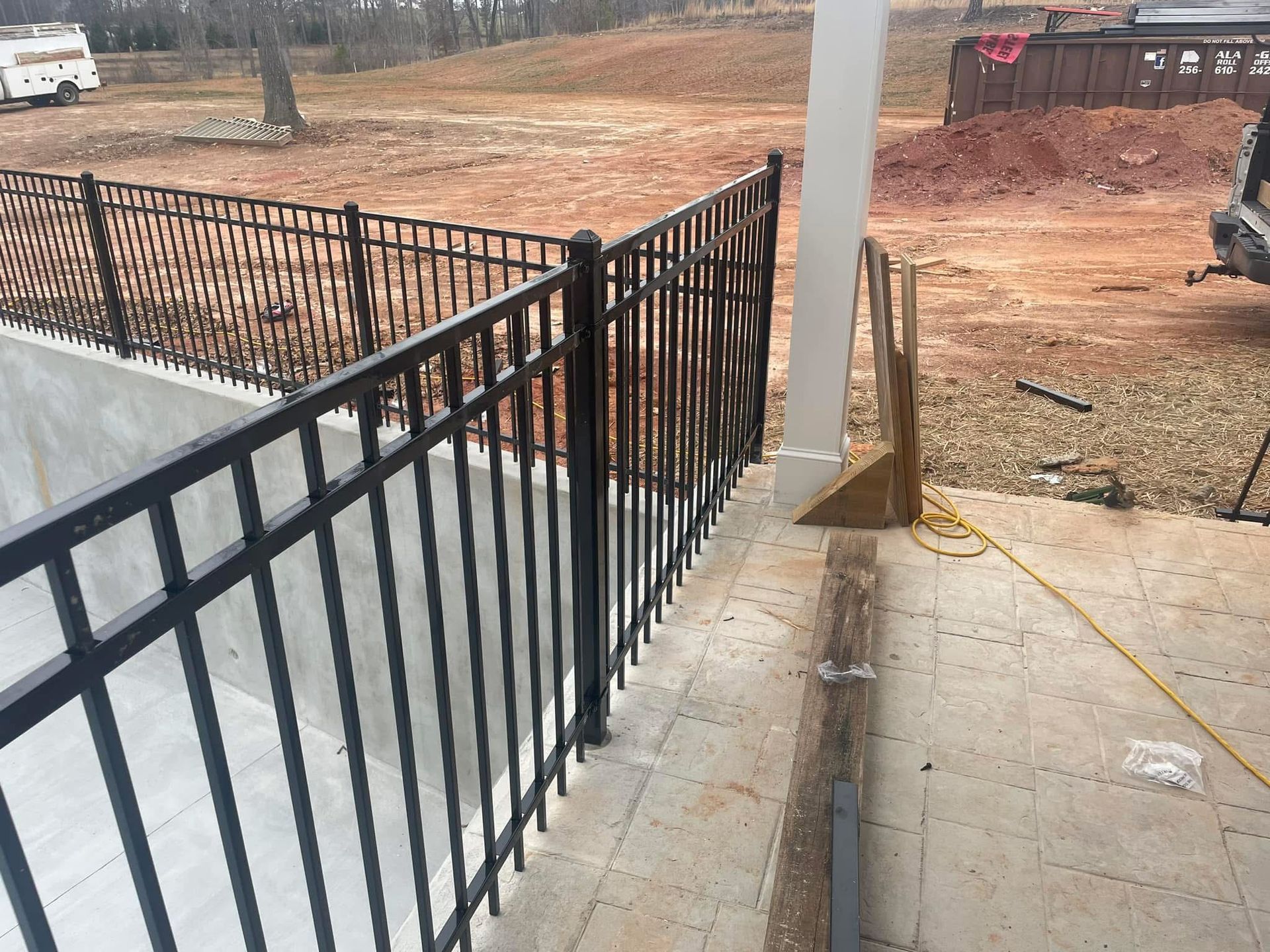 Black metal railing along a concrete porch beside a bare dirt lot and white support post
