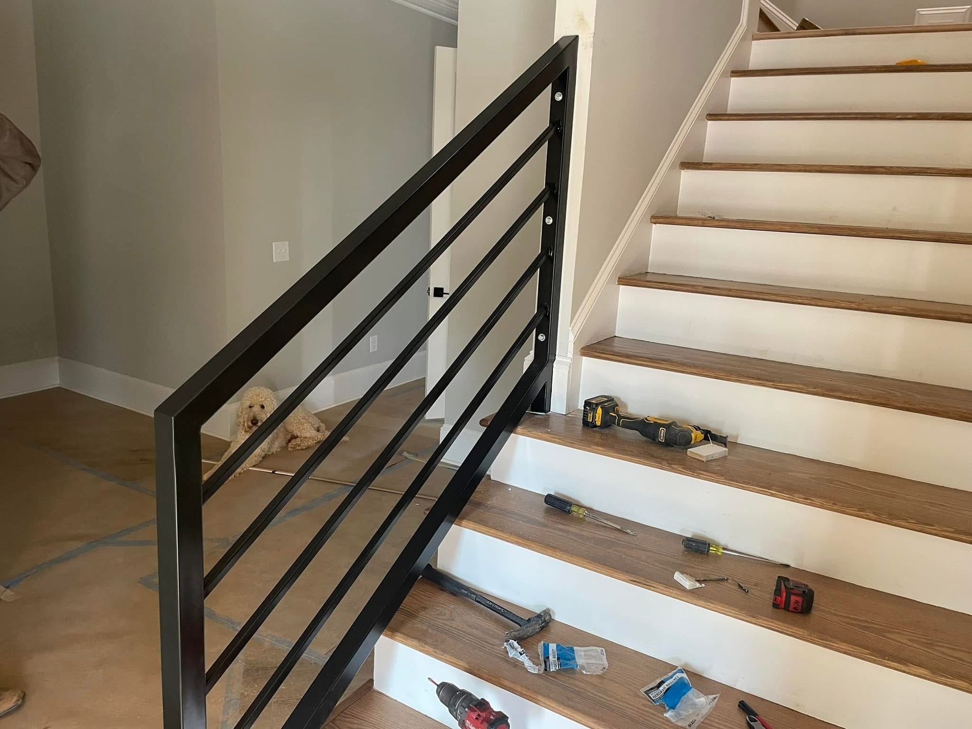 Staircase with black railing and light wood steps, scattered tools and items on the stairs.