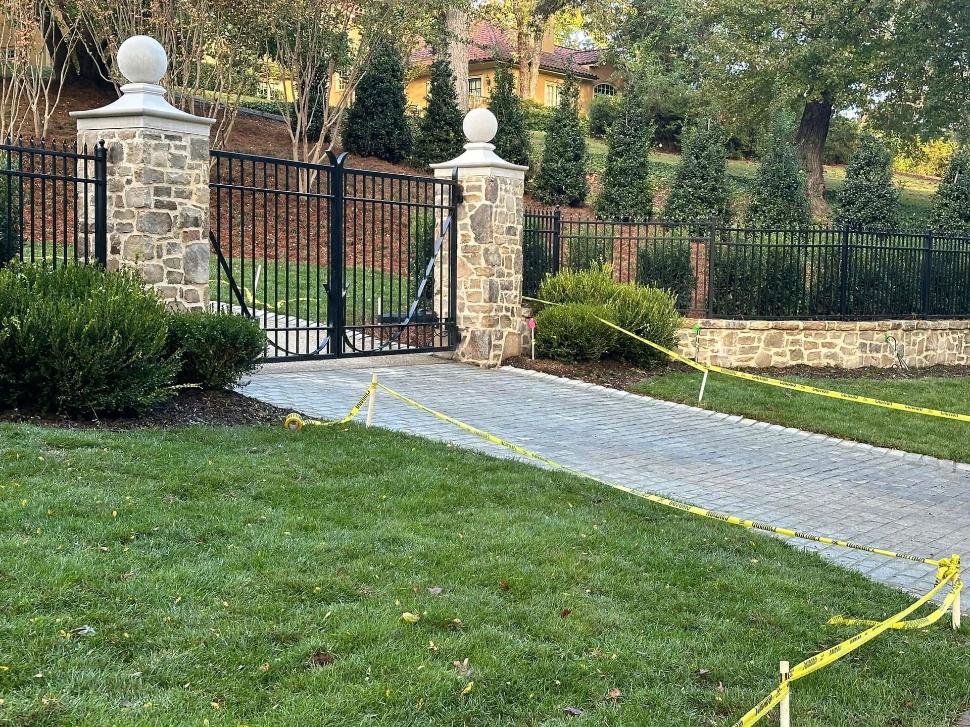 Stone gate and black iron fence beside a curved gravel path across a green lawn.