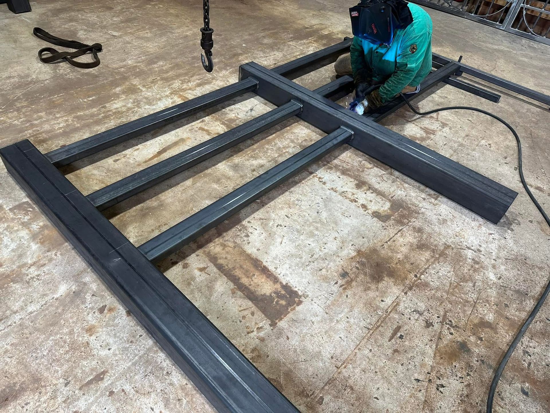 Person welding a black metal frame on a concrete floor in a workshop