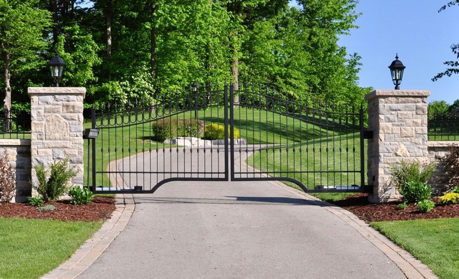 Wrought-iron gate between stone pillars at the entrance to a landscaped driveway