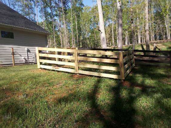 Wooden slatted fence in a grassy yard beside a house, with trees in the background.