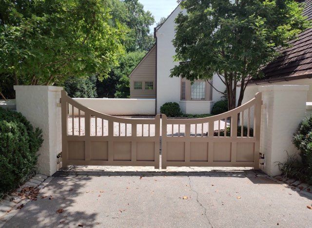 Beige wooden driveway gate with brick pillars in front of a house and trees