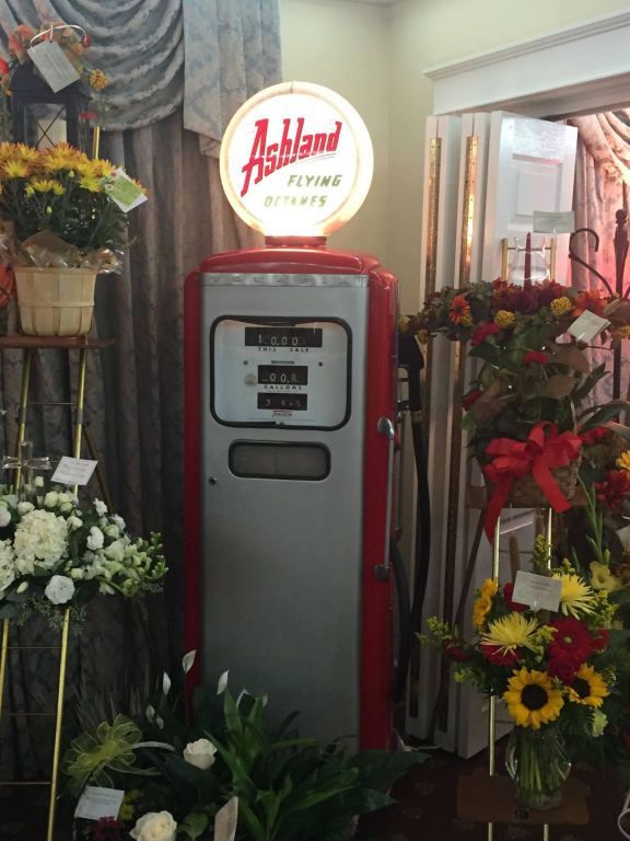 An ashland gas pump is surrounded by flowers in a room