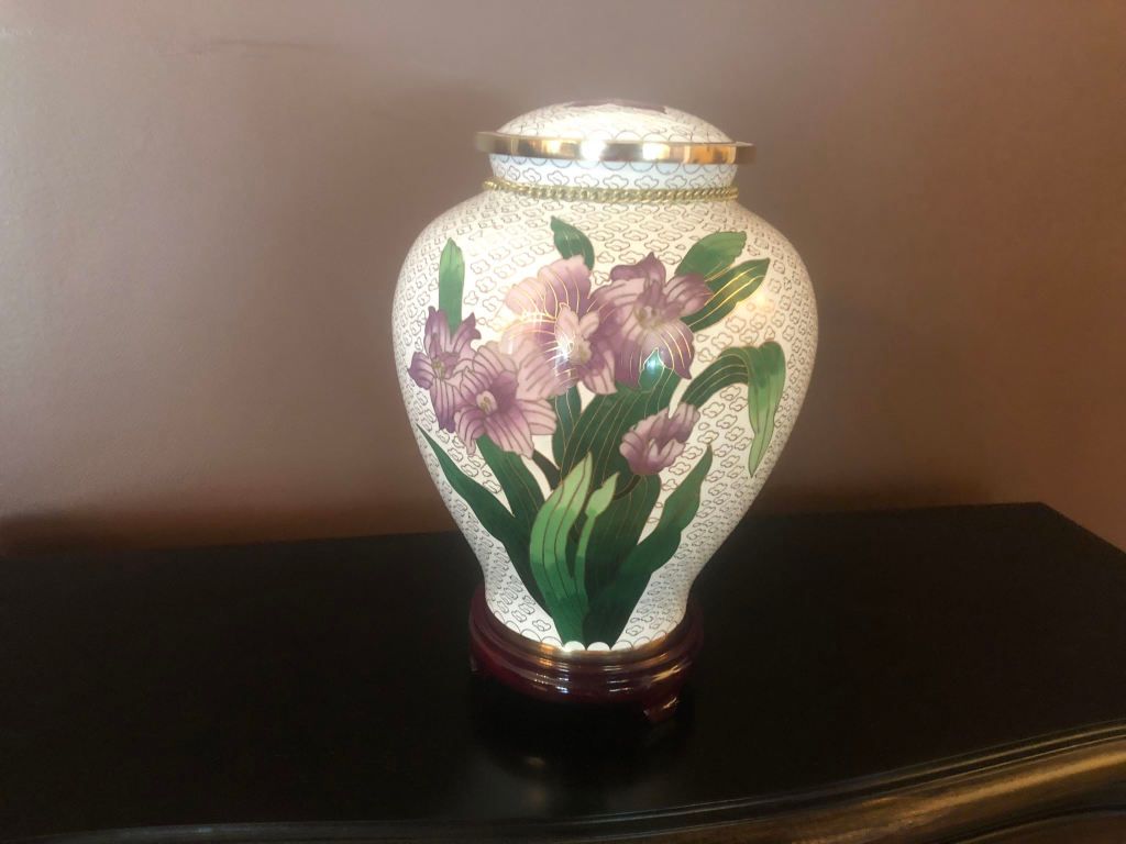 A white urn with purple flowers painted on it is sitting on a table.